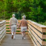 Older couple walking hand in hand across a wooden bridge