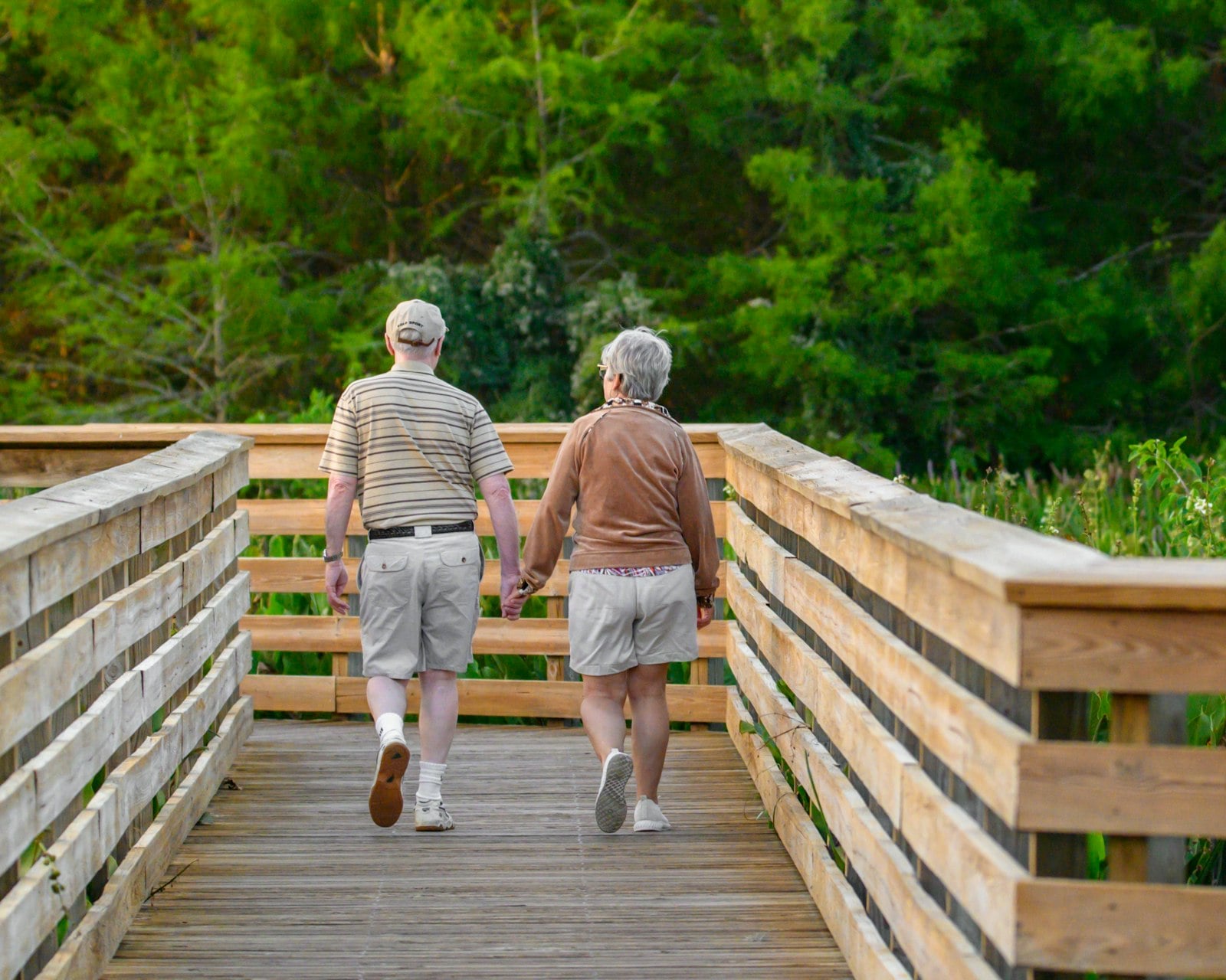 Older couple walking hand in hand across a wooden bridge